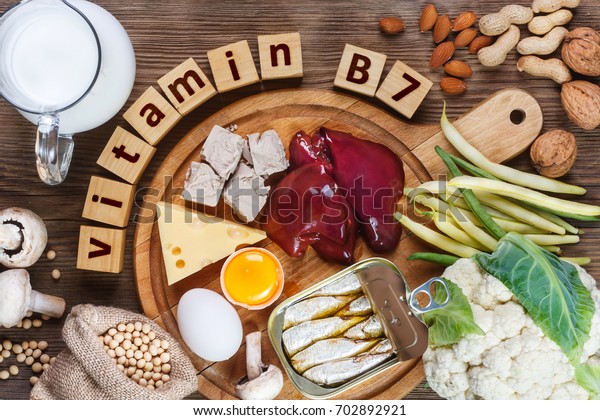 Voedingsmiddelen die rijk zijn aan vitamine B7 (biotine). Voedingsmiddelen zoals lever, eigeel, gist, kaas, sardines, sojabonen, melk, bloemkool, groene bonen, champignons, pinda's, walnoten en amandelen op houten tafel