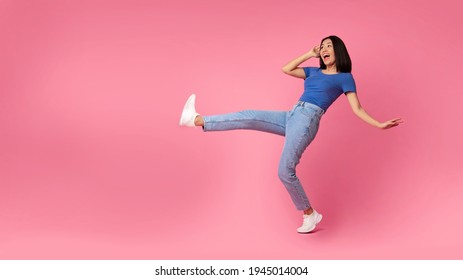 Fooling Around. Full Length Shot Of Ecstatic Young Asian Lady Jumping, Dancing And Raising Leg Up, Being In A Good Mood, Celebrating Victory, Bright Pink Studio Background, Free Copy Space, Panorama