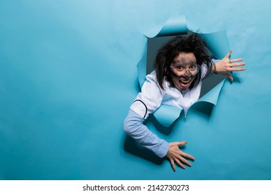 Foolish Humorous Scientist With Comic Expression On Blue Background. Young Adult Chemist With Wacky Look, Messy Hair And Dirty Face Acting Goofy After Experiment Explosion. Studio Shot.