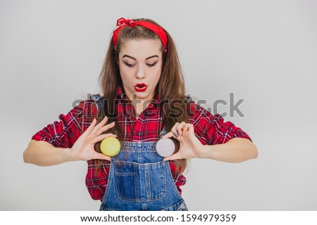Foolish young playful girl is holding two macaroons on the place of the buttons of her jeans. Expressive look.