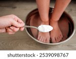 Foot baths in hot water. A woman puts a spoonful of soda in the water