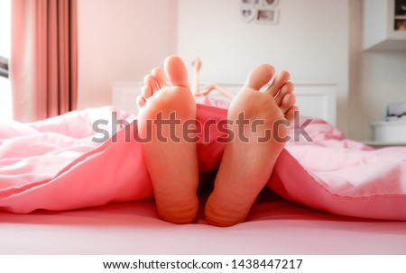 Foot in Bed at Home, Sleeping & Relax. Two Feet on the Bed in Pink Bedclothes. Beautiful Young Woman Barefoot in Bedroom Background. Female Feet is Lying fall Asleep on Pastel Bed Covered in Morning.
