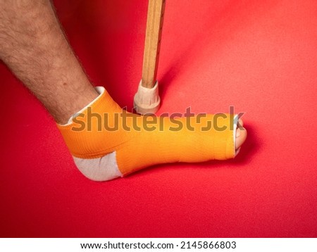 Foot with broken toe bone in orange fiberglass cast pink background. Injured fractured swollen male leg in modern orthopedic waterproof cast made of synthetic thermoplastic glass cloth. Patient body.