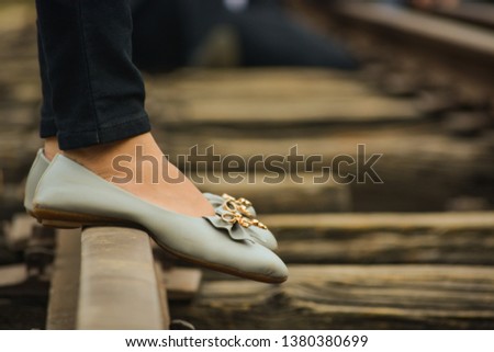 Foot (feets) of a girls standing on a railway track wearing grey coloured bellies with a golden flower on it. Old fashioned railway tracks.