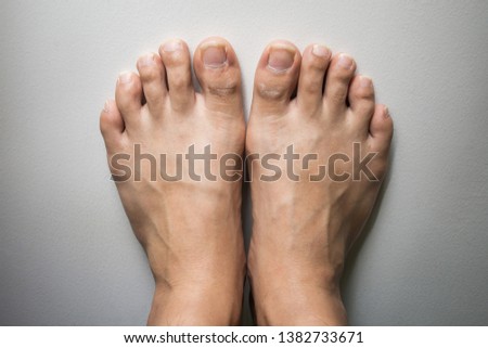 The foot and long nail toes on white concrete background. Long nails and dirty may cause fungal.