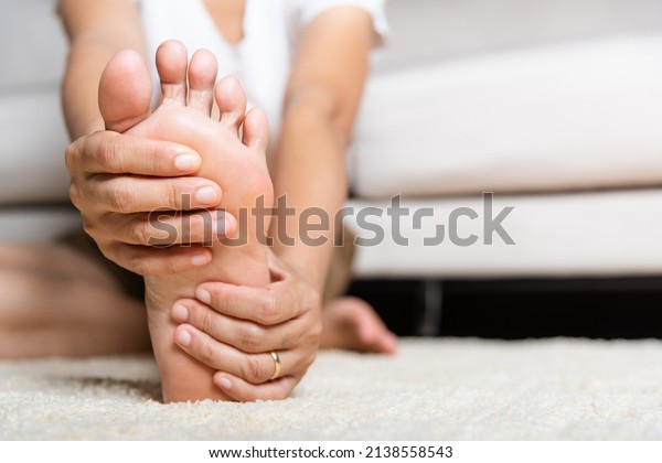 Foot pain, Asian woman feeling pain in her foot\
at home, female suffering from feet ache use hand massage relax\
muscle from soles in home interior, Healthcare problems and\
podiatry medical concept
