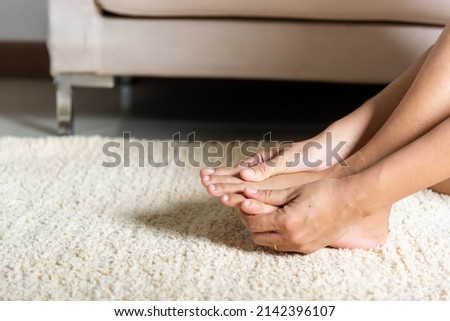 Foot pain, Asian woman holds her toe injury feeling pain her foot at home, female suffering from feet ache use hand massage relax muscle from toe in house interior, Healthcare problems medical concept