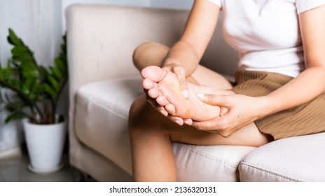 Foot pain, Asian woman sitting on sofa feeling pain in her foot at home, female suffering from feet ache use hand massage relax muscle from soles in home interior, Healthcare and podiatry medical - Shutterstock ID 2136320131