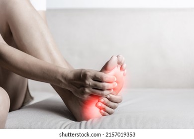 Foot pain, Asian woman sitting on sofa feeling pain in her foot at home, female suffering from feet ache use hand massage relax muscle from soles in home interior, Healthcare and podiatry medical - Shutterstock ID 2157019353