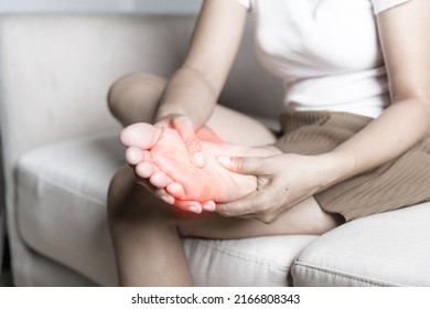 Foot pain, Asian woman sitting on sofa feeling pain in her foot at home, female suffering from feet ache use hand massage relax muscle from soles in home interior, Healthcare and podiatry medical