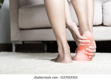 Foot pain, Asian woman standing feeling pain in her foot at home, female suffering from feet ache use hand massage relax muscle from soles in home interior, Healthcare problems and podiatry medical - Shutterstock ID 2157019355