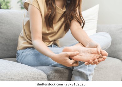 Foot pain concept, close up hand of young woman rubbing, massaging sore feet area of pain, girl suffering on sofa, couch at home. Discomfort painful feet ache from walking for long. Physical injury.