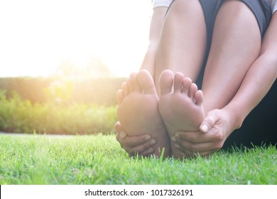 Foot Pain Leg Of Beauty Woman Sitting On The Road Park Holding Her Feet And Stretch The Muscles In Morning Sunlight .Health Care And Spa Concept.