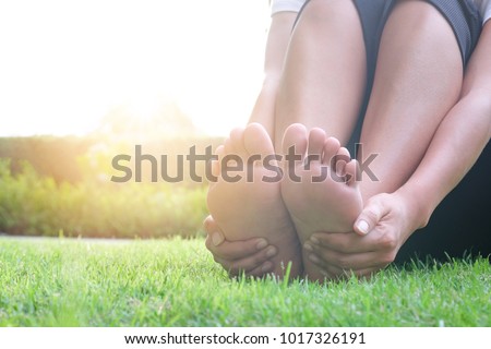 Foot Pain Leg of beauty woman sitting on the road park holding her feet and stretch the muscles in morning sunlight .Health care and spa concept.