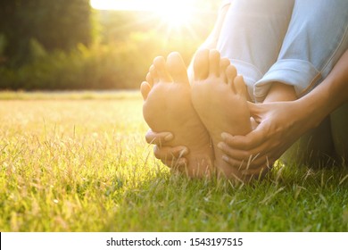 Fußschmerz Leg des Menschen sitzend auf Gras im Park halten die Füße und dehnen die Muskeln in der Morgensonne .Gesundheit und Spa Konzept.