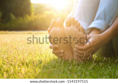Foot Pain Leg of man sitting on grass in the park holding he feet and stretch the muscles in morning sunlight .Health care and spa concept.