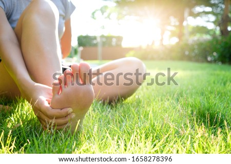 Foot Pain Leg of woman sitting on grass in the park holding he feet and stretch the muscles in morning sunlight .Health care and spa concept.