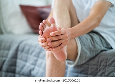 Foot pain, man suffering from feet ache in home interior, podiatry concept - Shutterstock ID 2013306155