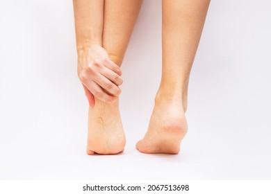 Foot Pain From Uncomfortable Shoes. Female Feet With Flaky Skin And Corns Isolated On A White Background. A Woman Holds A Sore Heel With Her Hand. Pathology Of Bone Structures, Flat Feet. Orthodontics