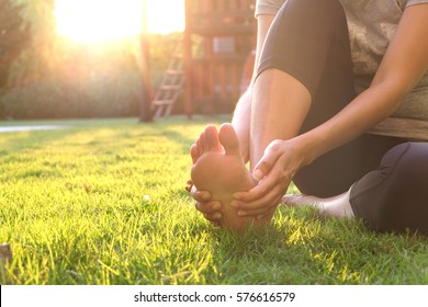 Foot pain .Woman sitting on grass Her hand caught at the foot. Having painful feet and stretching muscles fatigue To relieve pain. health concepts. - Shutterstock ID 576616579