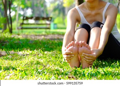 Foot Pain .Woman Sitting On Grass Her Hand Caught At The Foot. Having Painful Feet And Stretching Muscles Fatigue To Relieve Pain. Health Concepts.