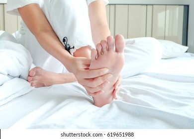 Foot Pain Woman Sitting On The Bed Holding Her Feet At Home Having Painful Feet And Stretching Muscles Fatigue To Relieve Pain. Health Concept.