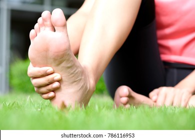 Foot Pain Woman Sitting On The Grass Holding Her Feet. Health Concept.