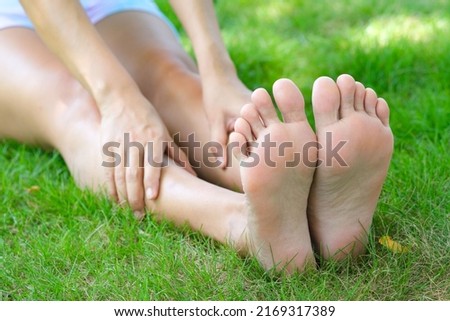 Foot pain .Woman sitting on grass Her hand caught at the foot. Having painful feet and stretching muscles fatigue To relieve pain. health concepts.