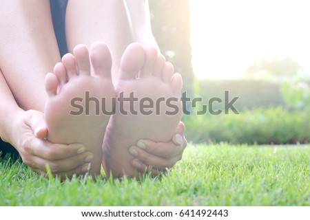 Foot pain .Woman sitting on grass Her hand caught at the foot. Having painful feet and stretching muscles fatigue To relieve pain. health concepts.