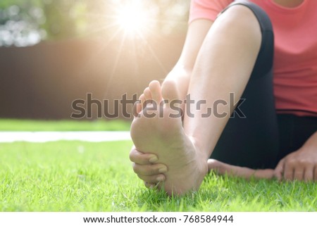 Foot Pain woman sitting on the grass holding her feet. Health concept.