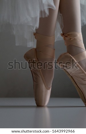 Foot in a peach ballet shoe pointe on white surface.