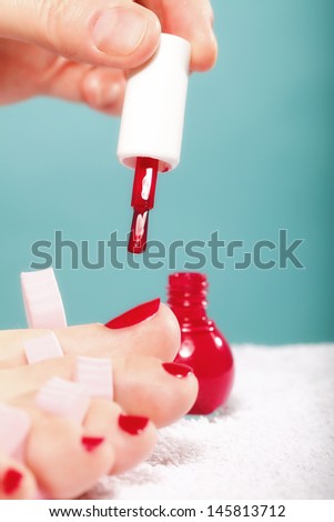 foot pedicure applying woman's feet with red toenails in pink toe separators blue background