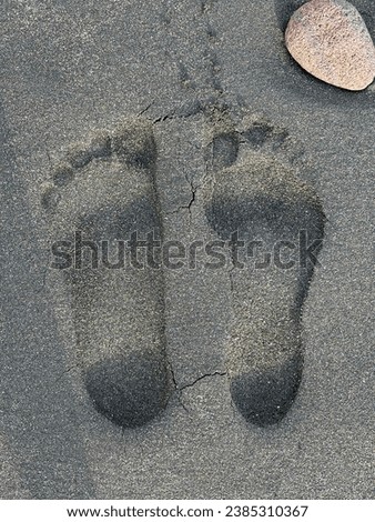 Foot prints of wife and husband on a black sand beach in New Zealand by Pacific Ocean front.