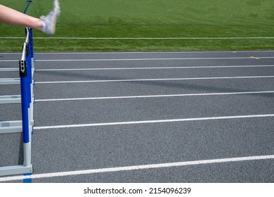 a foot shows motion as it leaps over an off center track and field running hurdle on an athletic track with lane markings shot in natural light with copy space - Powered by Shutterstock