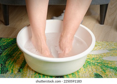 Foot soaking. Woman put hot water for her feet. Homemade bath soak for dry feet skin. Female feet with spa bowl.