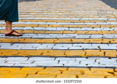 A Foot Wrapped In Sandals Takes A Step Along A Pedestrian Crossing On A Stone-paved Road