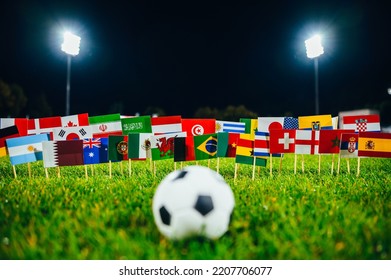 Football Ball On Green Grass And All 32 National Flags. Soccer Game, Wallpaper With Black Edit Space. Football Tournament And Stadium