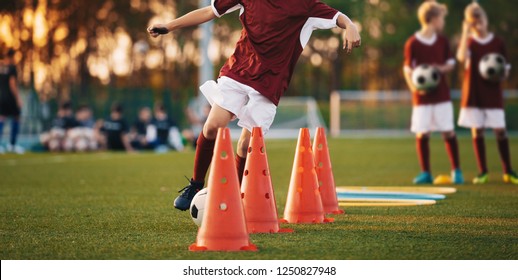 Football Drills: The Slalom Drill. Youth soccer practice drills. Young football players training on pitch. Soccer slalom cone drill. Boy in red soccer jersey shirt running with ball between cones