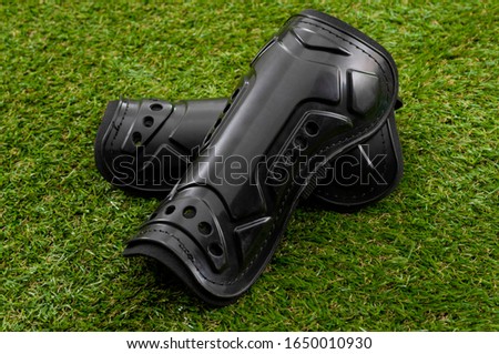 Football equipment, injury and bruise prevention and soccer gear concept with tough black shin guards isolated on grass background