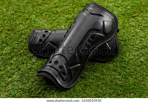 Football equipment, injury and bruise\
prevention and soccer gear concept with tough black shin guards\
isolated on grass\
background
