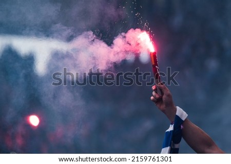 Football fan burns flare in the hand with scarf at the stadium