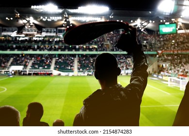 Football fan celebrating a goal of his favorite team with raised hands and club scarf