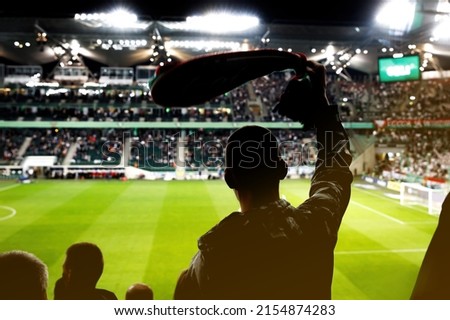 Football fan celebrating a goal of his favorite team with raised hands and club scarf