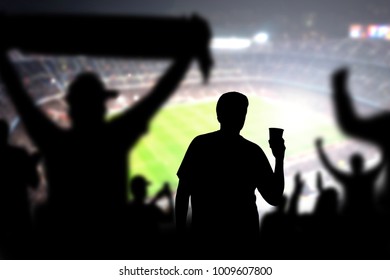 Football Fan Drinking Beer In Crowd In Stadium. Man With Alcohol Beverage In Soccer Audience At A Game. Holding Pint. Drunk Person In Live Sport Event. Silhouette People Watching Match In Arena.