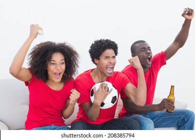 Football Fans In Red Sitting On Couch Cheering On White Background