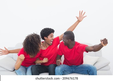 Football Fans In Red Sitting On Couch Cheering At Home In The Living Room