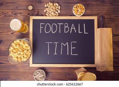 football fans setting of beer bottle in brown paper bag,  glass, chips, pistachio and handwriting text football time written in chalkboard over wooden table, flat lay - Powered by Shutterstock