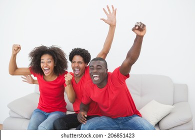 Football fans sitting on couch cheering together at home in the living room - Powered by Shutterstock