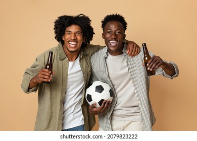 Football Fans. Two Cheerful Black Guys Holding Soccer Ball And Drinking Beer, Having Fun Together On Beige Background, Excited Happy African American Male Friends Cheering Favorite Team, Free Space