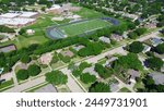 Football field in middle school district surrounding by residential houses lush green trees, swimming pool, well-trimmed grassy front yard, upscale neighborhood in suburbs Dallas, aerial view. USA